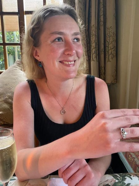 Lilley sits smiling with candle light reflected on her face. On the ring finger of her right hand, a silver Irish Claddagh ring inlaid with small diamonds and sapphires is visible. The design is of a heart, with two hands (one on either side of the heart) and a crown (above the heart), and the heart's point faces inwards.
